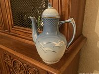 Front view of the Bing and Grondahl blue and white porcelain coffeepot with seagull relief and gold accents.