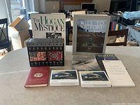 Books and VHS set arranged on a table; six visible books including The Hogan Mystique, Will to Victory (autographed), Harvey Penick golf book, Messerschmitt ME262, two Boeing history books, with PBS Civil War VHS episodes 1-9 box and two boxes of notecards.