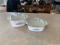 Photo of two white rectangular Corningware casserole dishes with blue cornflower decorative pattern and clear glass lids
