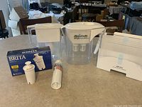 Photo of fridge ice bin replacement and various water filtration pitchers and filters on table.