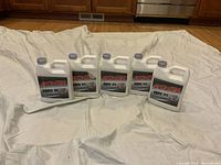 Five 1-quart bottles of KYB motorcycle oils on white cloth, three labeled Fork Oil 01M unopened, one Fork Oil 01M half full, and one K2C Shock Oil unopened.
