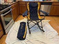 Blue and gold MAC Sports rocking camp chair set up on kitchen floor with included matching carrying bag beside it.