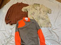 Lot of three men's long-sleeve shirts: rust patterned Tommy Bahamas shirt, light yellow floral Kahala silk short sleeve shirt on hanger, gray and bright orange Clarkfield Outdoors shirt with Henrys logo