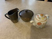 Photo shows three pieces: Noritake Elements collection creamer, matching sugar bowl with lid, and a separate ceramic teapot with colorful geometric patterns.