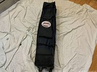 Dark blue Quik Shade instant canopy stored in black wheeled carrying bag laying flat on a surface. Bag bears the Quik Shade logo and front pocket, shows overall good condition.
