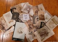 Overview photo showing all 25 antique cabinet card photos spread out on a wooden surface, varied sizes and some photos mounted on cards.