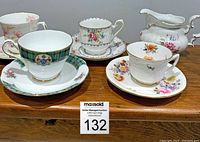 Four bone china teacups and saucers and bone china creamer arranged on wooden surface, showing unique patterns and styles for each set