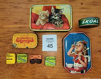 Eight vintage tins arranged on wood surface showing candy tins with kittens and girl blowing bubbles, tobacco tins Erinmore and Skoal, and four fuse tins.