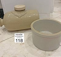 Side view of antique Langley Ware foot warmer and small stoneware crock on tile floor