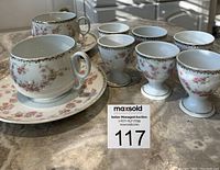 Full view of 6 egg cups, 2 tea cups, and 2 saucers on marble surface in natural light