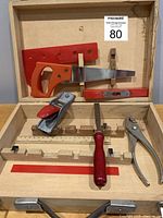 Full view of open wooden box containing child's woodworking tools: large saw, miniature saw, level, square, ruler, chisel, pliers, and hand plane.