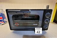 Front view of the DeLonghi Fan Convection Toaster Oven showing the black and white exterior, front window panel and control knobs.
