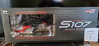 Front view of unopened Aero-G S-107 remote control helicopter in original packaging box with clear window showing helicopter inside.