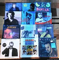 Top view of 12 sealed vinyl records arranged in a grid showing album covers from artists like Luther Vandross, Herman's Hermits, Earth, Wind & Fire, Mitsou, Dottie West, Blind Date soundtrack, and others.