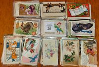 Several piles of individual postcards laid out on a wooden table, showing a variety of holiday and floral designs