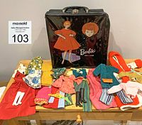 Photo of vintage black Barbie doll case with vintage red-haired Barbie illustration on front, shown with assorted Barbie doll clothing and accessories spread out.