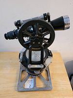 Front view of vintage surveyor's transit level showing base, leveling bubble and scope with adjustment wheel.