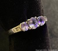 Close-up photo showing three medium purple oval amethyst stones set horizontally in a 10k gold band with diamond accents on each side.