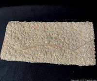 Closed view of a rectangular clutch bag densely covered in hand sewn pearls and seed beads in a floral and leaf pattern over cream fabric.