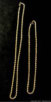 Two gold-toned rope chain necklaces of different sizes displayed on black background.