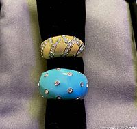Both rings shown with top view highlighting dome shape, cream enamel, gold-tone accents, and rhinestones; turquoise blue enamel ring with rhinestones also visible
