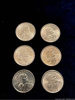 Obverse sides of six Sacajawea dollar coins from year 2000 arranged on dark fabric.