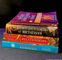 Stack of four astrology and spirituality books on a dark surface showing titles and covers.