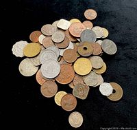 Large pile of assorted foreign coins on black background with a mix of metals, shapes, and visible engravings.