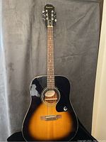 Full view of Epiphone acoustic guitar showing sunburst finish and black pickguard with Epiphone logo.