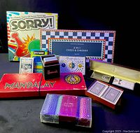 Shows various board games including Sorry!, Mandalay, 2-in-1 Chess & Checker, multiple decks of playing cards including Bee brand, Harwoods brand and others, plus a set of poker chips.