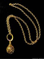 Full view of the gold tone chain necklace with attached round loop and filigree pendant against black background.