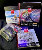 Photo showing three Arteza spiral-bound art pads with different paper counts and uses, along with a large resealable bag full of assorted markers.