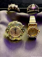Photo of two silver-tone fashion rings and two vintage ring watches on a dark cloth background