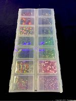 Full top view of plastic container with 12 compartments filled with assorted miniature craft beads including various colors and shapes
