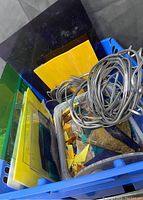 Bin with uncut sheets of colored stained glass (yellow, green, blue) and some coiled wire on top.