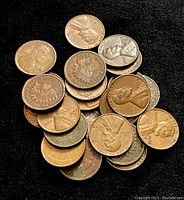 Overhead view of a pile of 20+ U.S. pennies including Indian Head, Wheat, and Lincoln pennies with visible dates ranging mostly from early to mid 1900s.