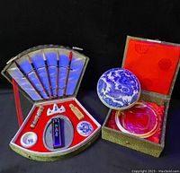 Full view of two vintage Asian ink kits. Left kit with brushes, ink stick, ink slab, small porcelain cups in fan-shaped case with red velvet lining. Right kit with blue dragon round ink container and circular ink slab in green patterned box with red interior.