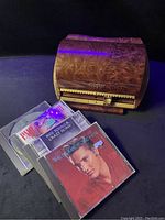 Closed vintage wooden Diskgear CD holder with textured swirl wood pattern finish next to several CDs lying flat