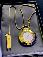 Front view of the gold tone Stilton quartz pocket watch showing the Roman numeral bezel and attached chain and clip.