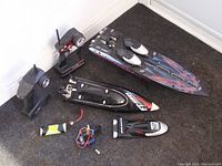Photo showing two RC boats, two remote controllers, battery pack, wiring and motor, and spare parts on carpeted floor