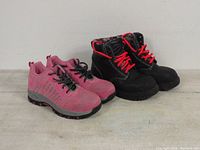 Side angle view showing the pink athletic safety shoes and black/red workboots together.