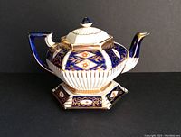 Front and side view of the hexagonal antique Staffordshire Imari teapot on matching trivet against black background.