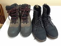 Two pairs of men's boots on table including brown and black Columbia hiking boots with red laces and black Dr Martens boots with yellow stitching around sole