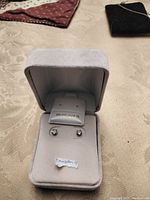 Two photos of genuine tanzanite stud earrings in 10k gold displayed in a light gray jewelry box with labels.
