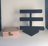 Photo showing both the closed pink vinyl jewellery box with key and the black three-tier bracelet holder side by side on a flat surface.