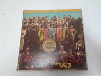 Front view of The Beatles Sgt Peppers Lonely Hearts Club Band album cover showing band members in colorful costumes with worn edges.