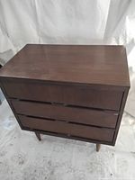 Front view of the dark wood small Mid-Century Modern dresser showing three drawers and tapered legs.