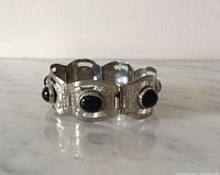 Front angle view of sterling silver bracelet with black onyx cabochons set in bezel surrounding overlapping hinged panels.