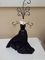 Front view of a black dress form jewelry holder standing on a white surface against a tan wall.