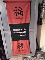 Wall hanging with Tibetan Good Luck characters and proverb hung on a vertical surface.